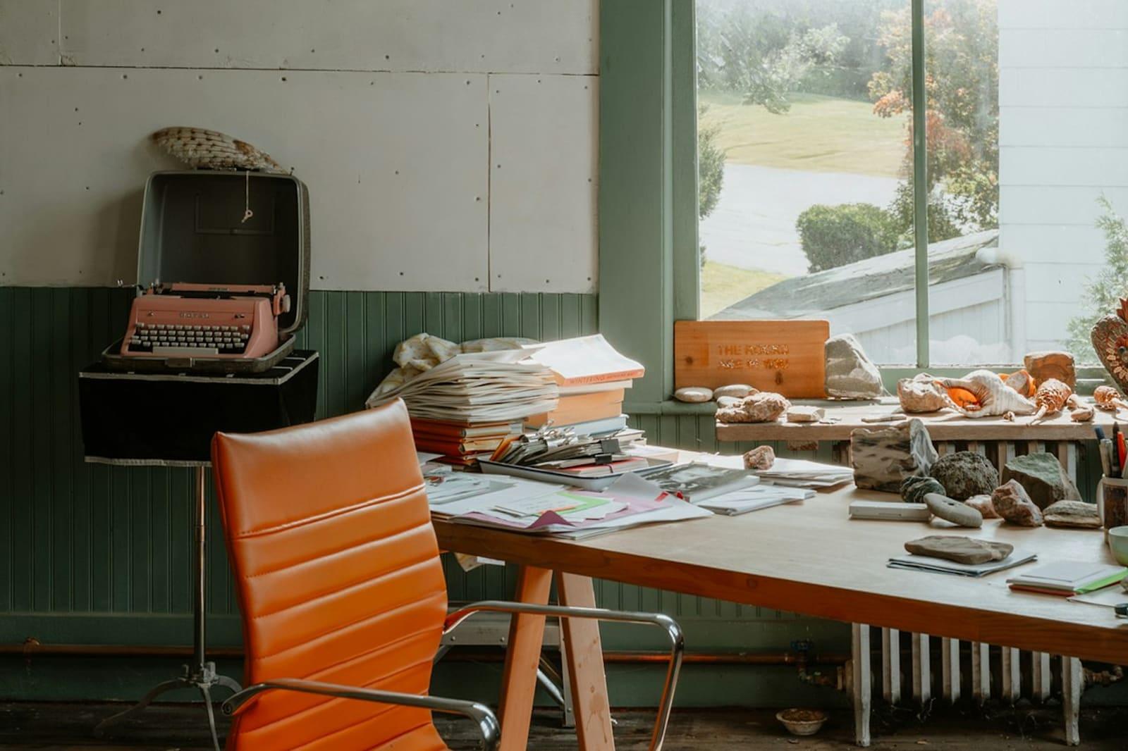 A studio desk with papers, a typewriter and a window.